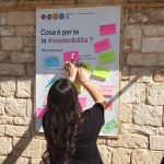 Partecipante ad attività di brainstorming attacca post-it con idee sulla sostenibilità su bacheca