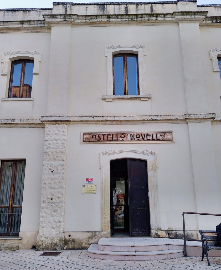 Facciata principale Ostello Novello di Novoli con 3 scalini, portone, insegna con la scritta Ostello Novello e finestra piano superiore