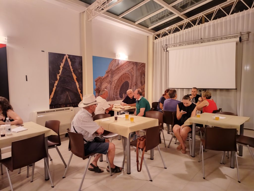 Un gruppo di persone è seduto nell’open space dell’Ostello Novello di Novoli, impegnato in conversazione.