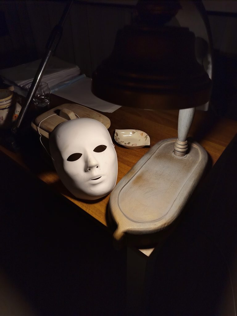 Dettaglio degli oggetti di scena dello spettacolo “I Fantasmi di Floyd” all’Ostello Novello una maschera bianca e una lampada da tavolo vintage