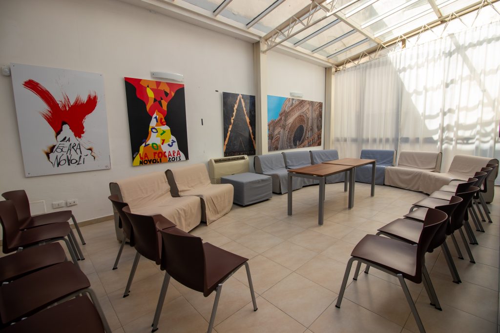 Vista prospettica della sala polifunzionale allestita con tavoli e sedie, pronta ad accogliere un momento di convivialità.
