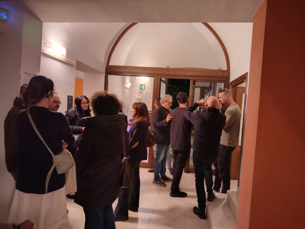 Gruppo di persone riunite dopo lo spettacolo “I Fantasmi di Floyd” all’Ostello Novello, mentre condividono opinioni e riflessioni sull’interpretazione di Lorenzo Di Lauro.