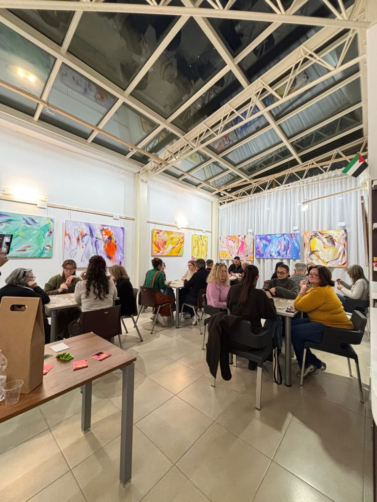 Persone sedute ai tavoli in una sala ampia e luminosa mentre partecipano al torneo di burraco.