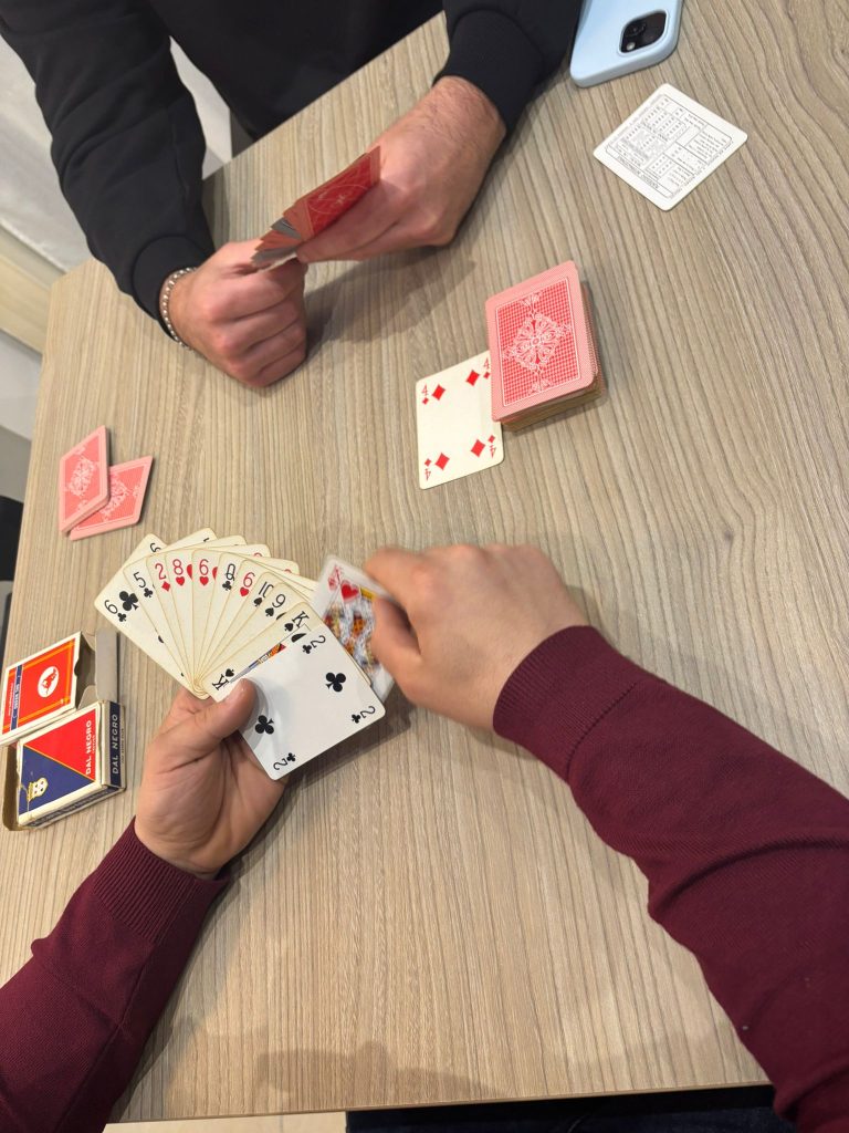 Diverse mani posano e muovono carte da gioco su un tavolo, durante una partita di burraco