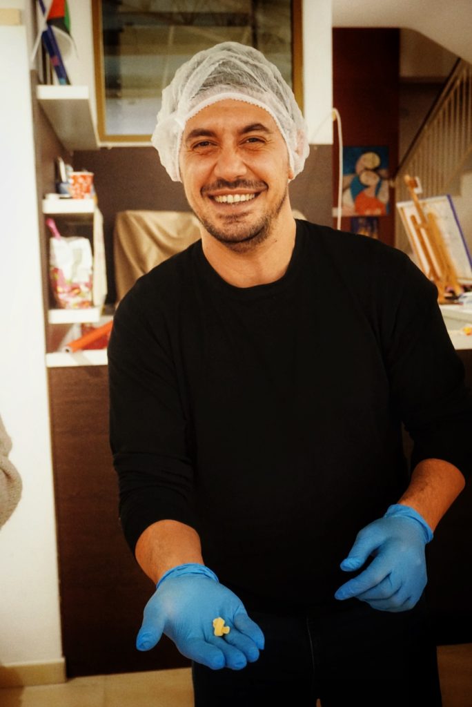 Persona con cuffia e guanti blu sorride all’interno dell’Ostello Novoli, durante un’attività pratica.